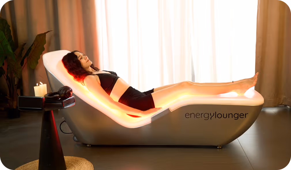 Woman in black sportswear relaxing on an illuminated Energy Lounger in a softly lit room with candles and plants.