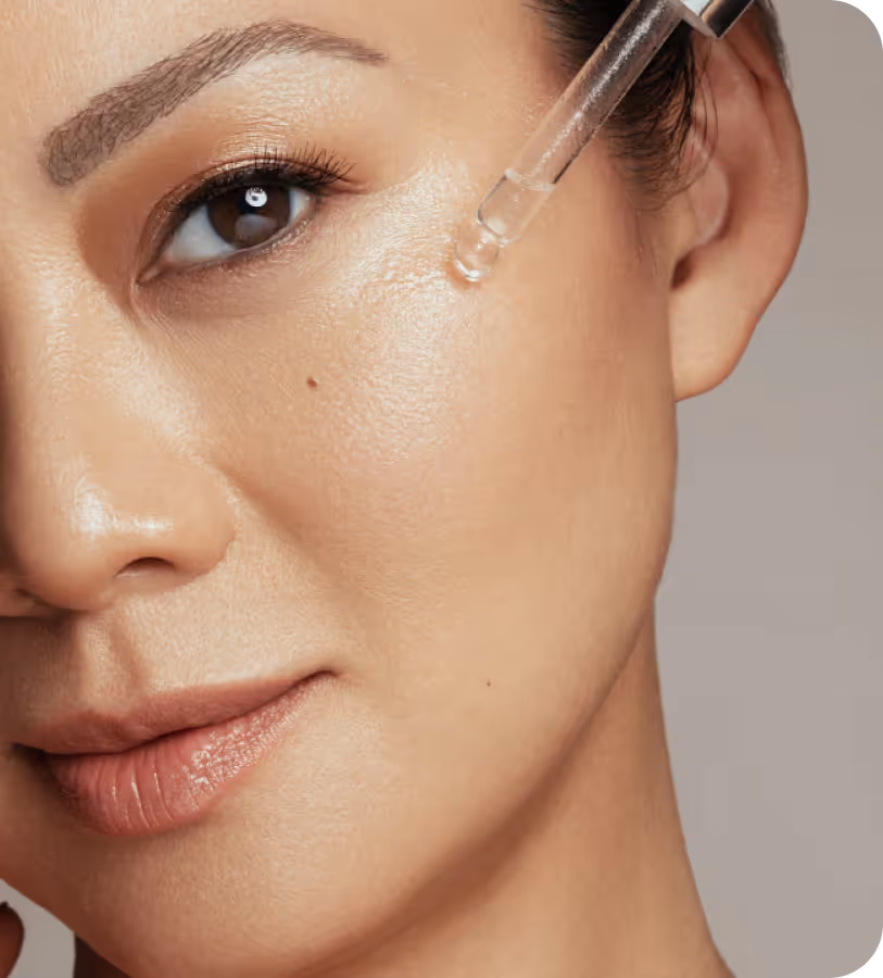 Close-up of a woman applying a clear serum drop to her cheek with a dropper.