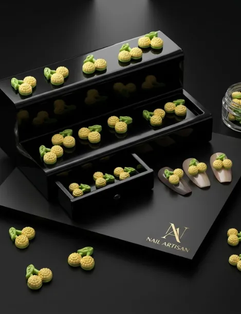 Yellow cherry-shaped nail charms with green stems displayed on black stands with Nail Artisan logo.