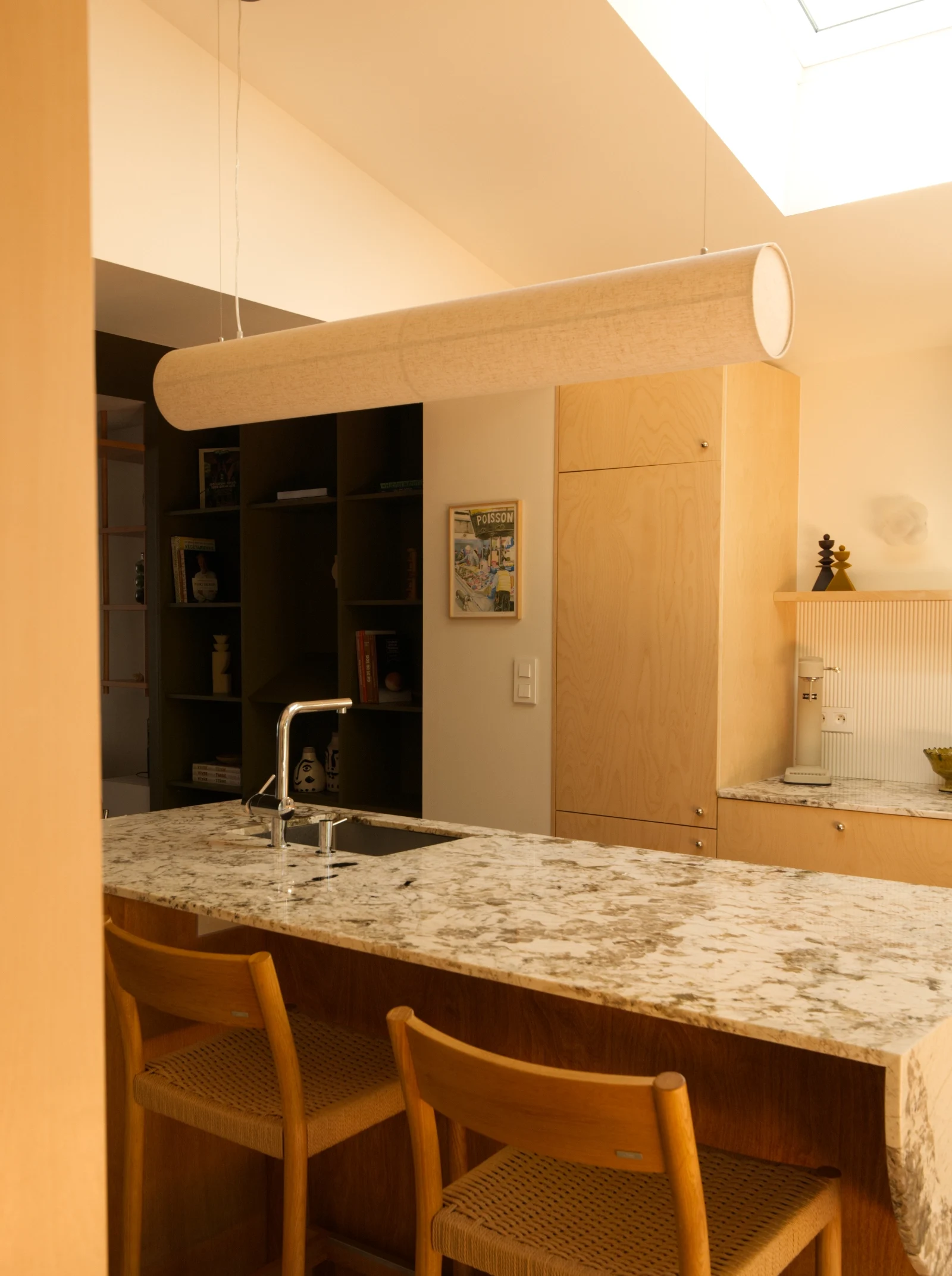 Vue de la cuisine et de la salle à manger du projet Léonard. Une structure en bois sur mesure, suspendue au plafond, délimite le salon sans cloisonner les espaces.