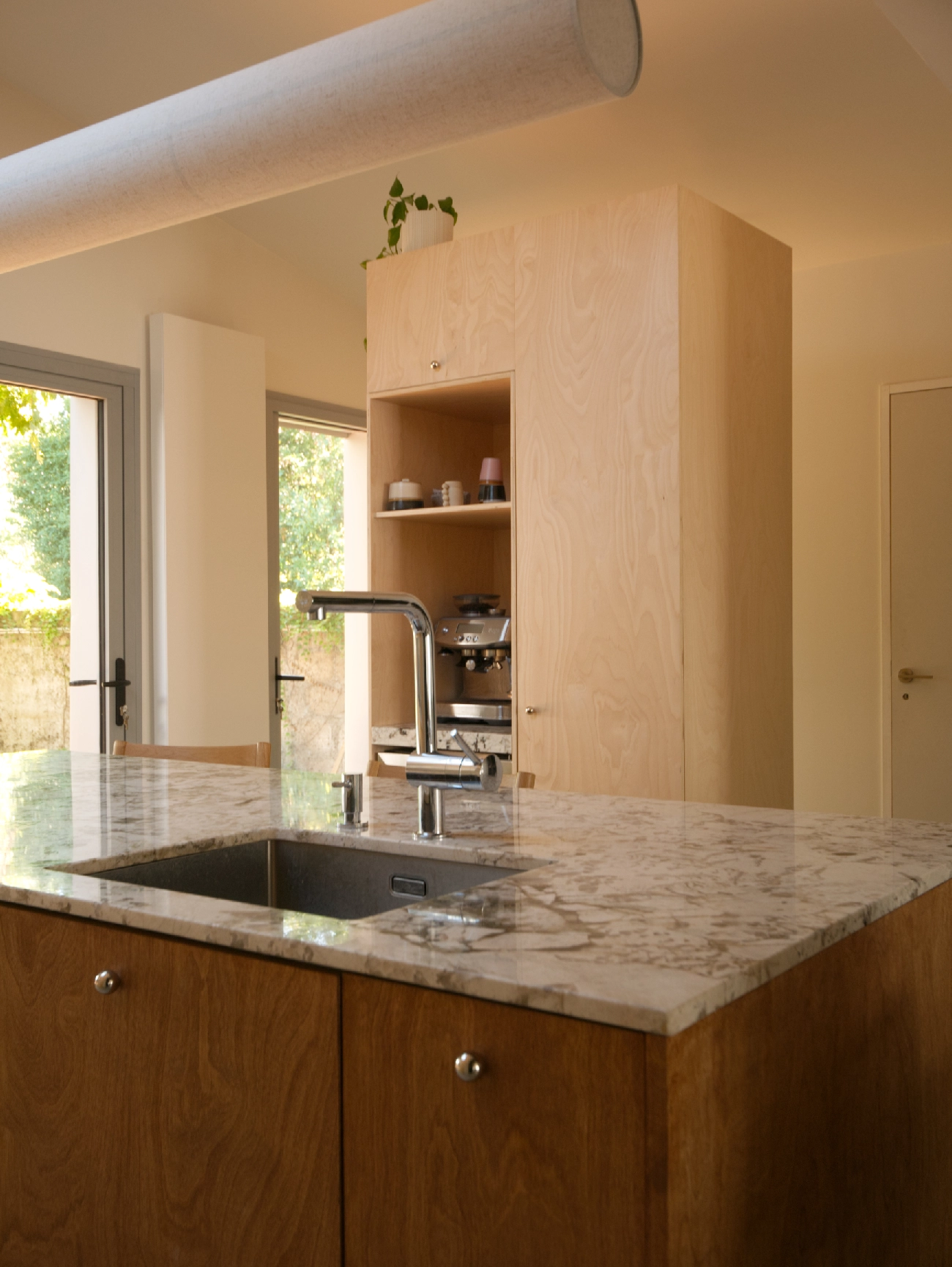 Dans cette cuisine, la colonne de rangement en bois n'est pas une colonne toute hauteur. L'espace libre laissé au-dessus permet de mettre en valeur des plantes pour réchauffer l'atmosphère tout en mettant à distance le plafond.