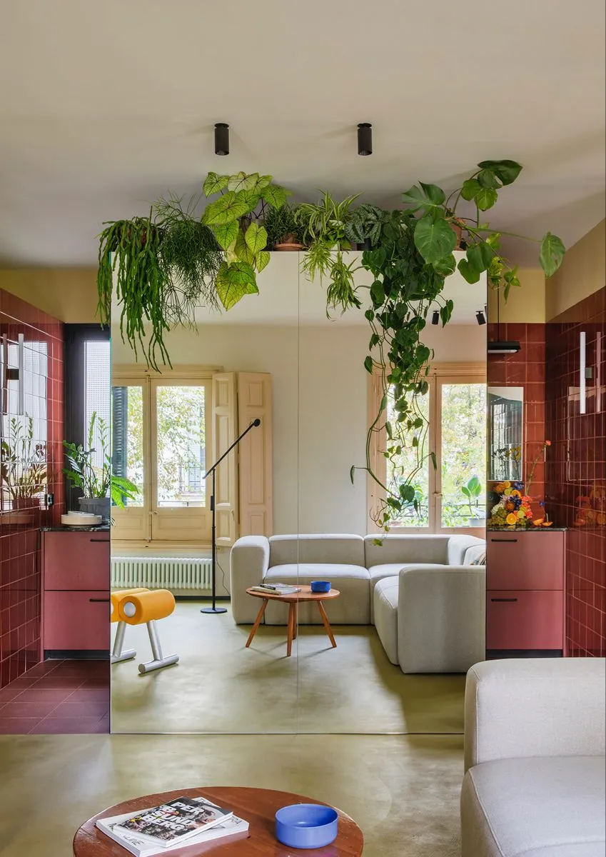 Dans cet appartement un meuble colonne magistral trône au centre de l'espace ouvert. Il sert de délimitation entre l'espace cuisine que l'on devine en arrière plan et le salon. Entièrement recouvert de miroir, il apporte une sensation d'espace immédiate dans la pièce en faisant entrer la verdure de la rue dans l'appartement.