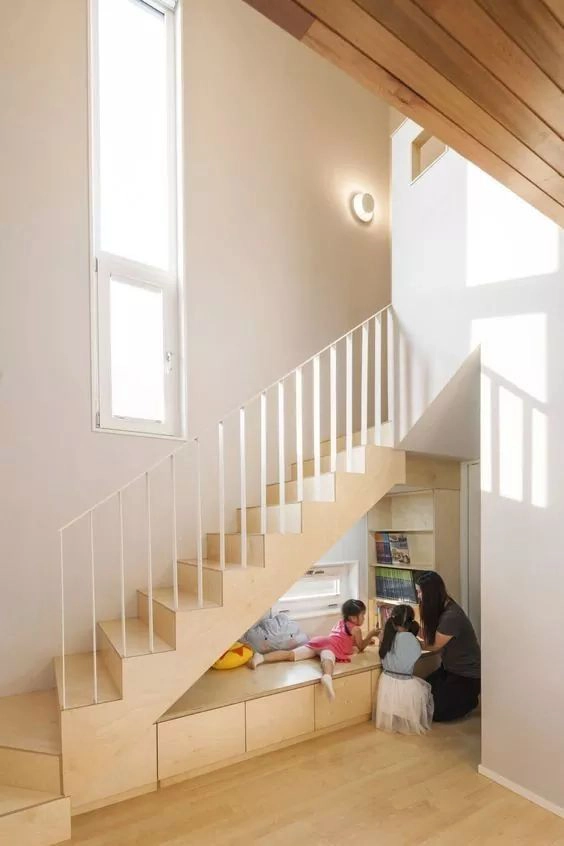 L'aménagement sous l'escalier offre un coin lecture aux enfants avec sa banquette et sa petite bibliothèque en bois clair.