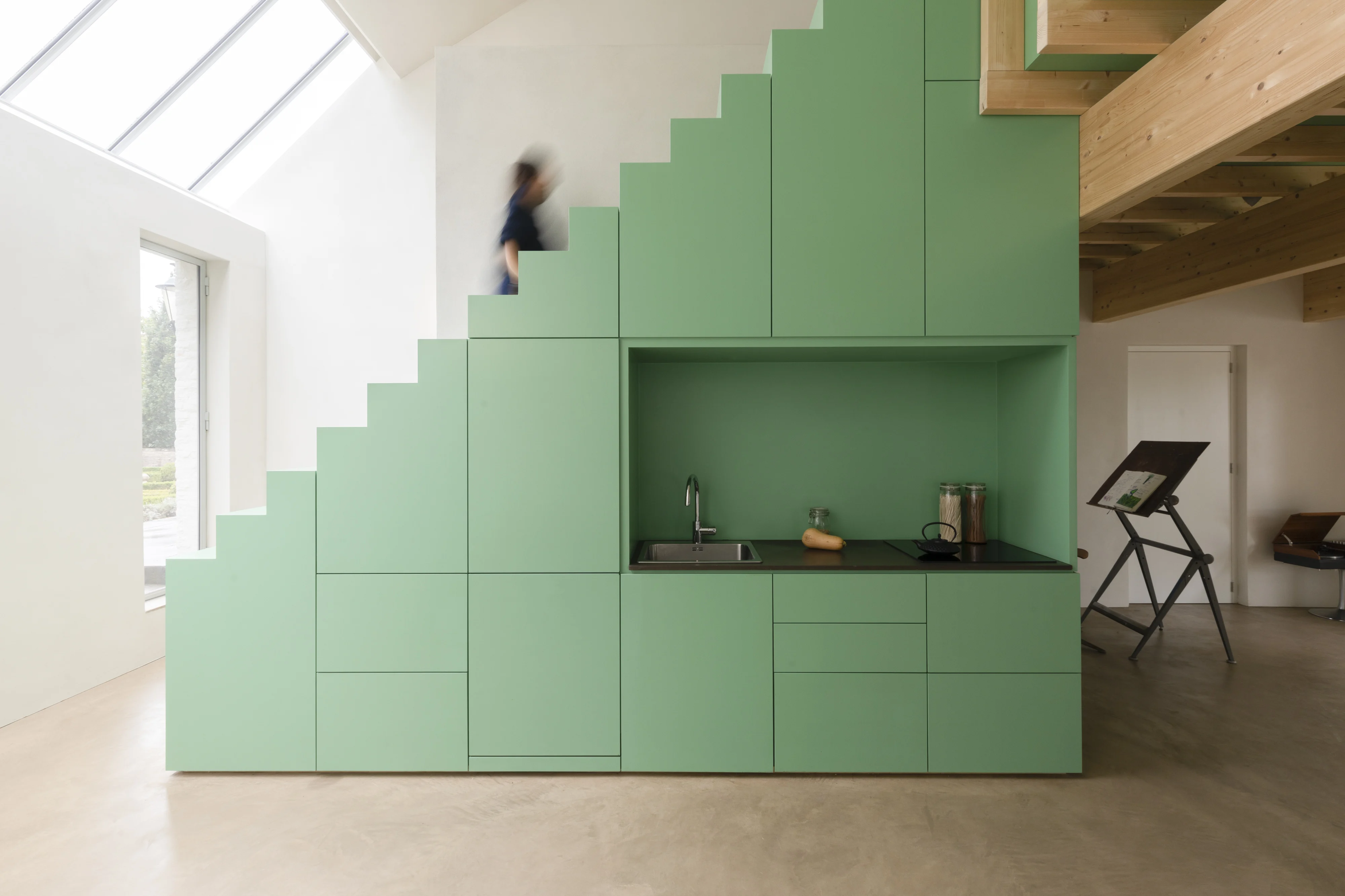 Pièce maîtresse de ce studio, cet agencement sur mesure intègre une kitchenette dans l'espace sous escalier avec de nombreux rangements fermés à fleur du limon.