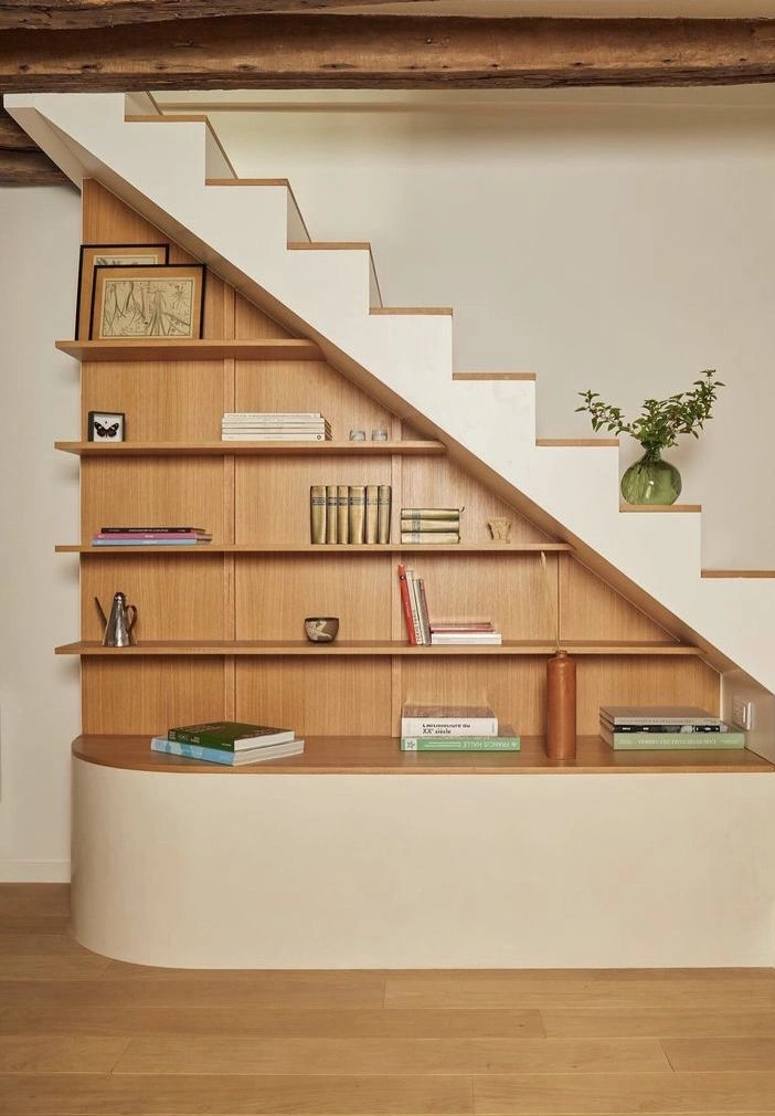 Une série d'étagères en chêne habillent le mur situé sous l'escalier. 