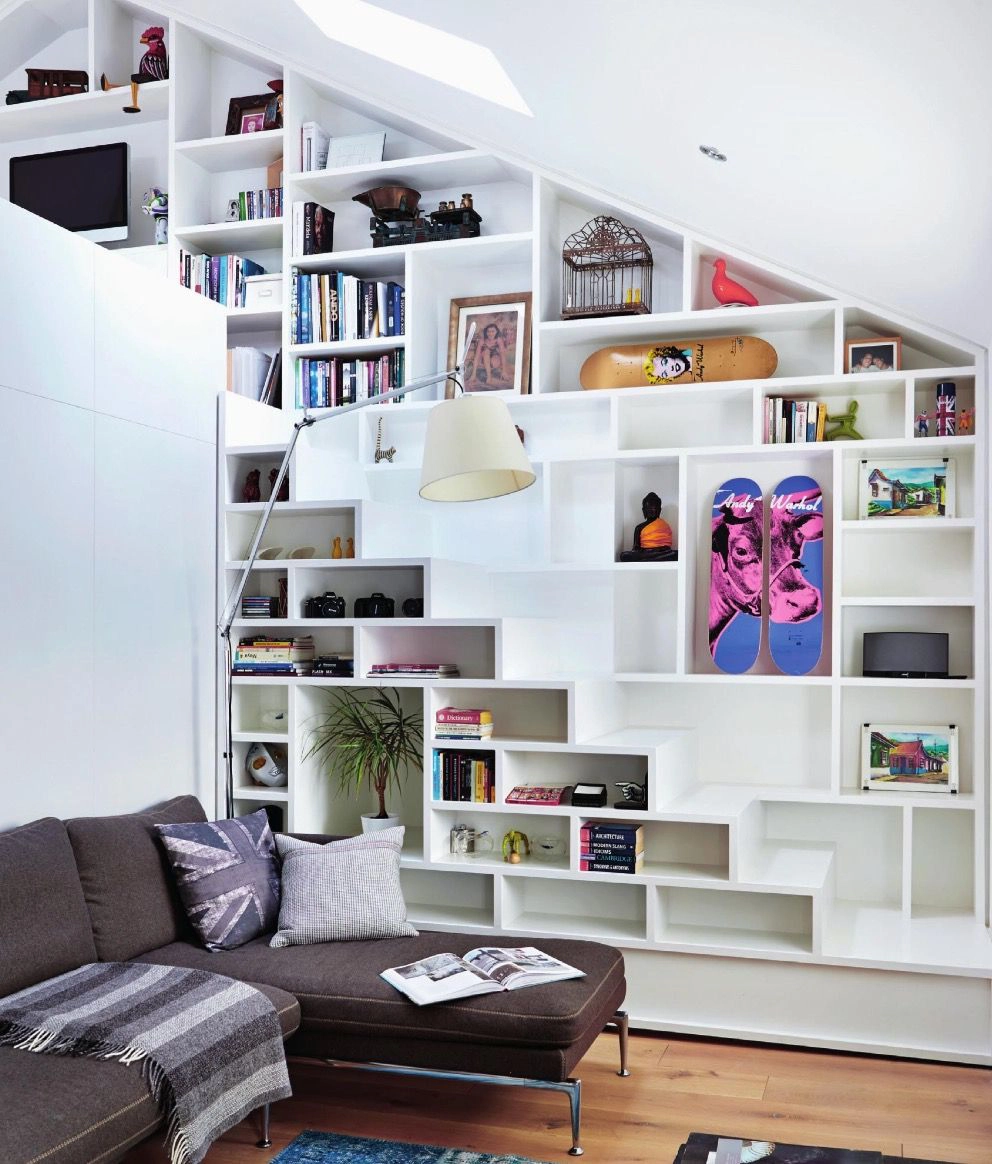 L'agencement de la bibliothèque forme un escalier. Le dessin de cette bibliothèque se poursuit sur le mur sur lequel est adossé l'escalier de manière à ce que l'escalier lui-même se fonde complètement dans la bibliothèque.