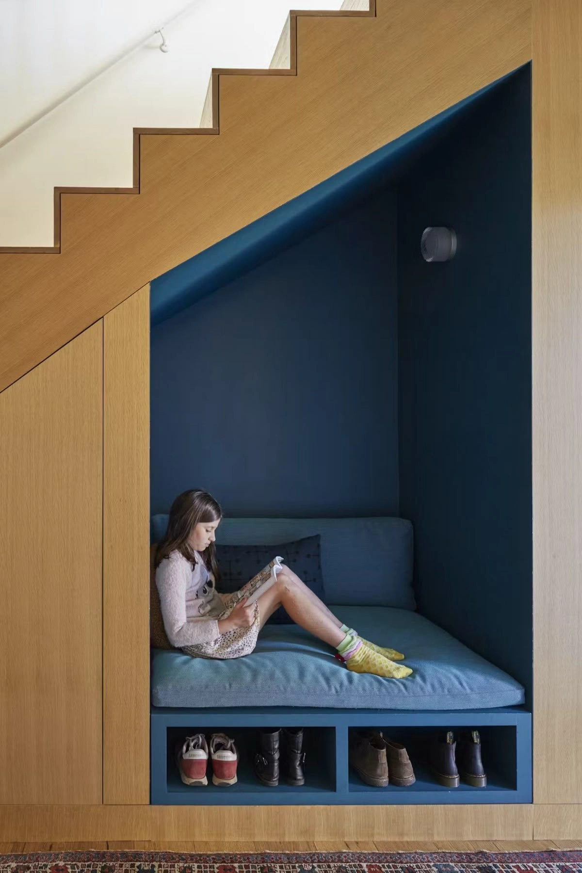 L'escalier de cette entrée accueille sous ses marches des rangements à chaussures surmontés d'une banquette pour se chausser