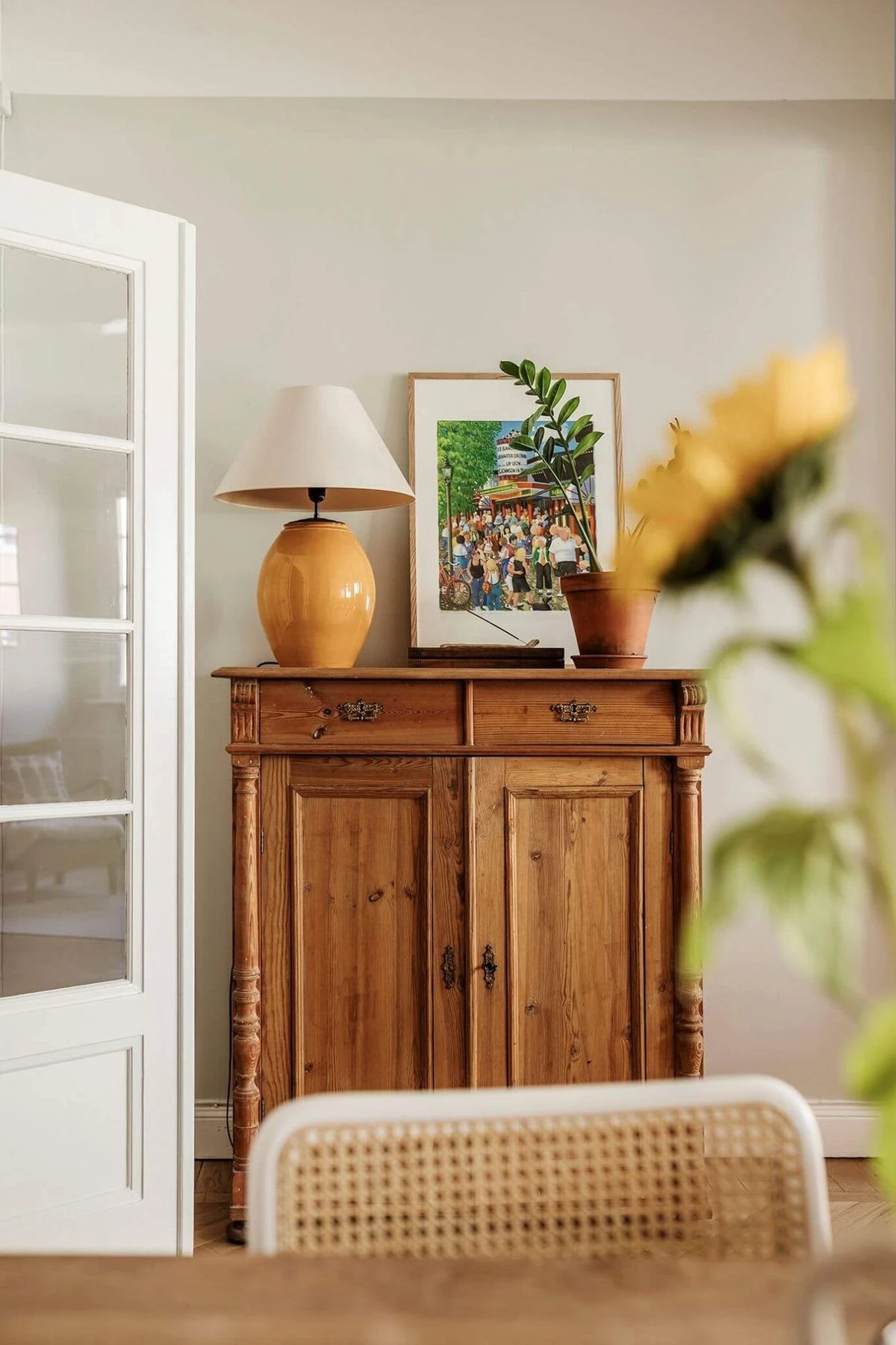 Dans un séjour épuré aux teintes douces, un buffet ancien en bois patiné est associé à une affiche murale colorée et contemporaine, créant un contraste équilibré entre mobilier d’époque et décoration actuelle.