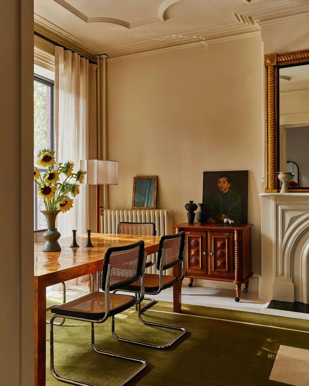 Des chaises modernistes de Marcel Breuer accompagnent une table ancienne dans une salle à manger aux murs clairs, avec un tapis vert contemporain.