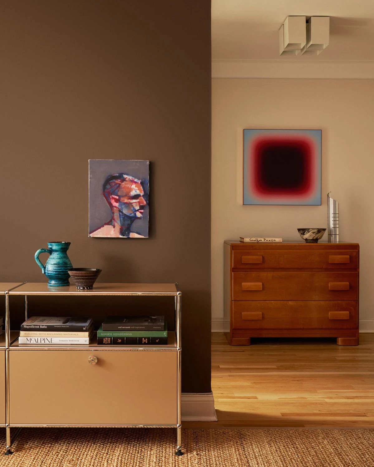 Deux commodes des années 60-70 se font face, l’une en métal et l’autre en bois, dans une pièce aux murs clairs et au mobilier sobre.