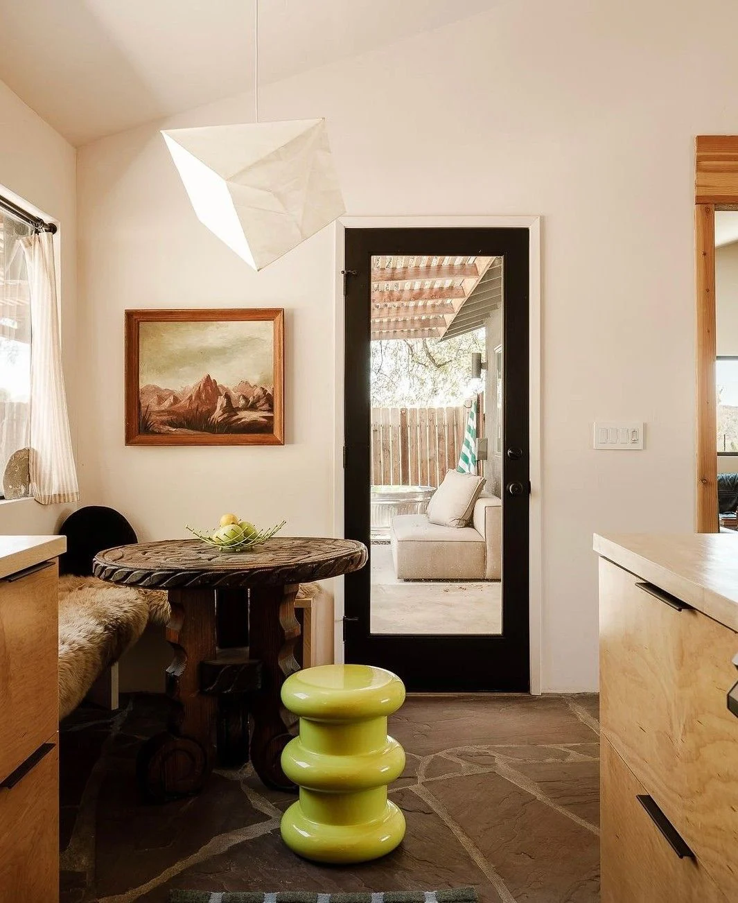 Un canapé vintage aux motifs fleuris prend place dans une chambre claire, sous une grande photographie contemporaine et à côté d’un tabouret rustique en bois.