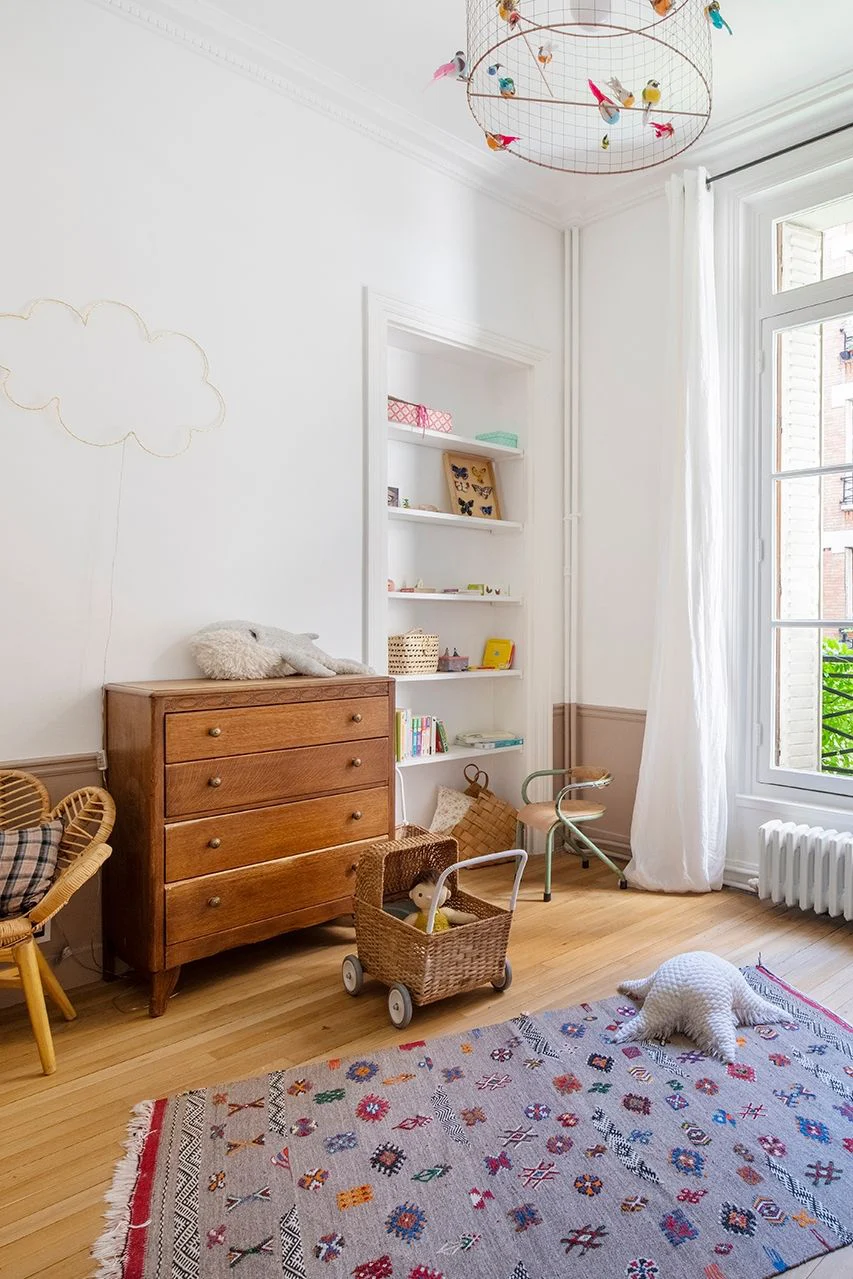 La commode ancienne en bois apporte beaucoup de charme à cette chambre d’enfant tandis que le tapis graphique, les jouets et les étagères ouvertes inscrivent l’espace dans une décoration actuelle.