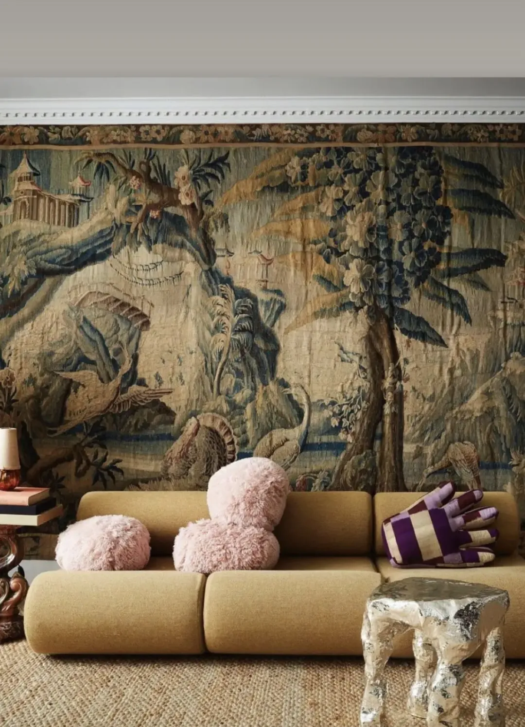 La tapisserie murale ancienne s’étend derrière le canapé contemporain et s’accompagne d’objets d’art, créant un contraste fort entre décor d’époque et mobilier actuel.