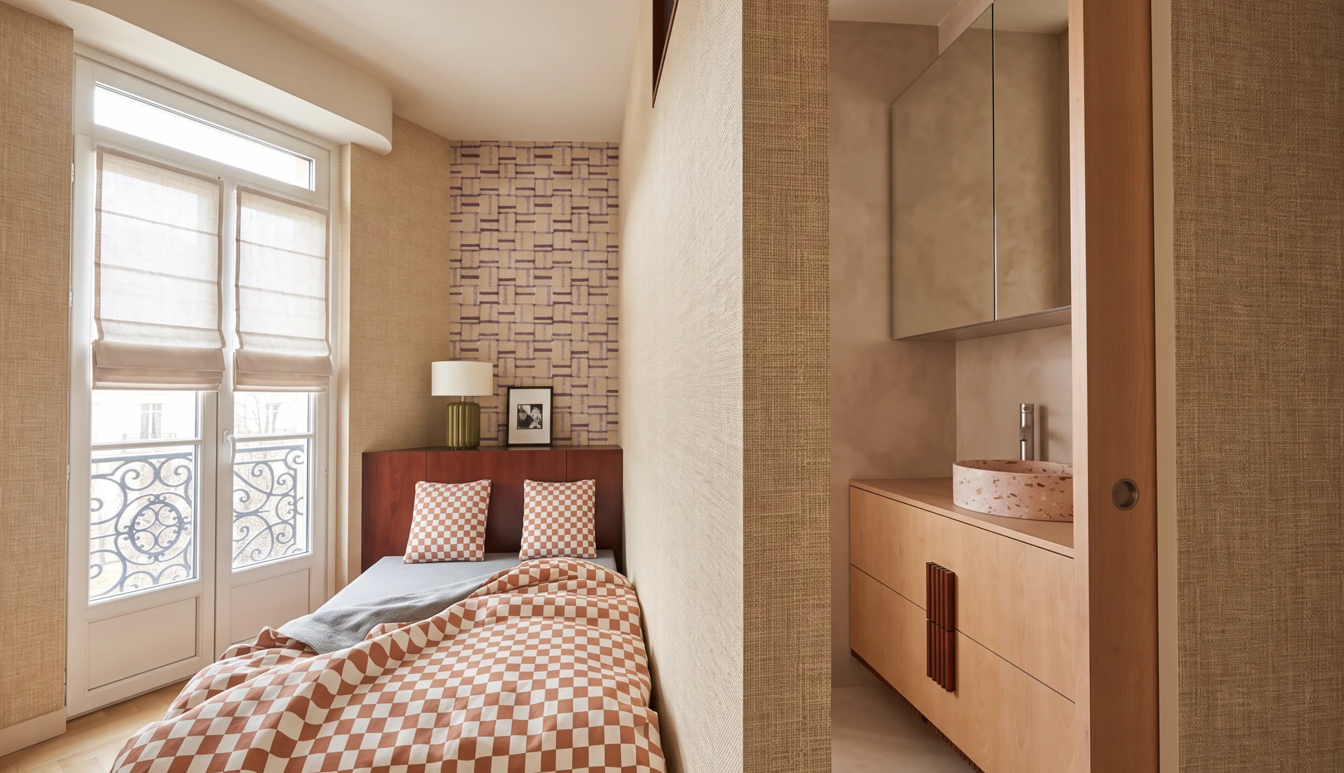 Chambre prolongée par une salle d'eau attenante : cloison en raphia, meuble vasque en bois clair, vasque en terrazzo rose et murs en enduit minéral beige.