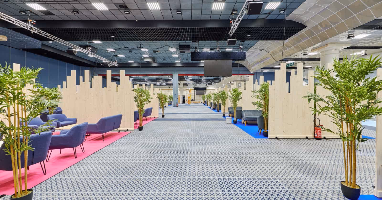Grand espace intérieur avec allée centrale, cloisons en bois, fauteuils bleus et plantes en pots.