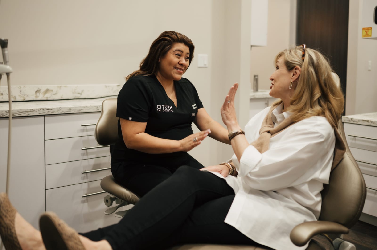 Dentist in black scrubs discussing treatment options with female patient in chair
