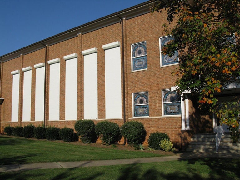 Brick building with white rolling shutters and greenery.