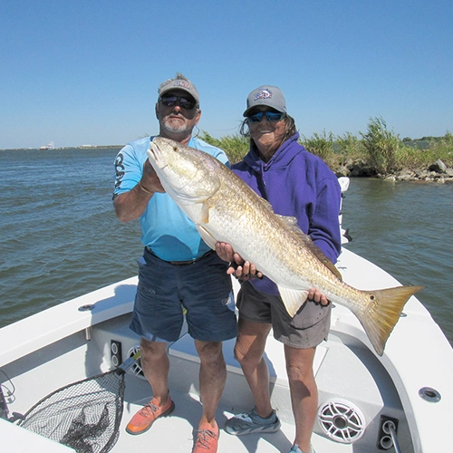 Two anglers holding large catch on boat with water and shoreline behind
