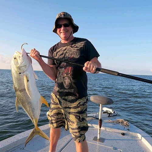 Smiling angler holding large yellow fish on boat with ocean background