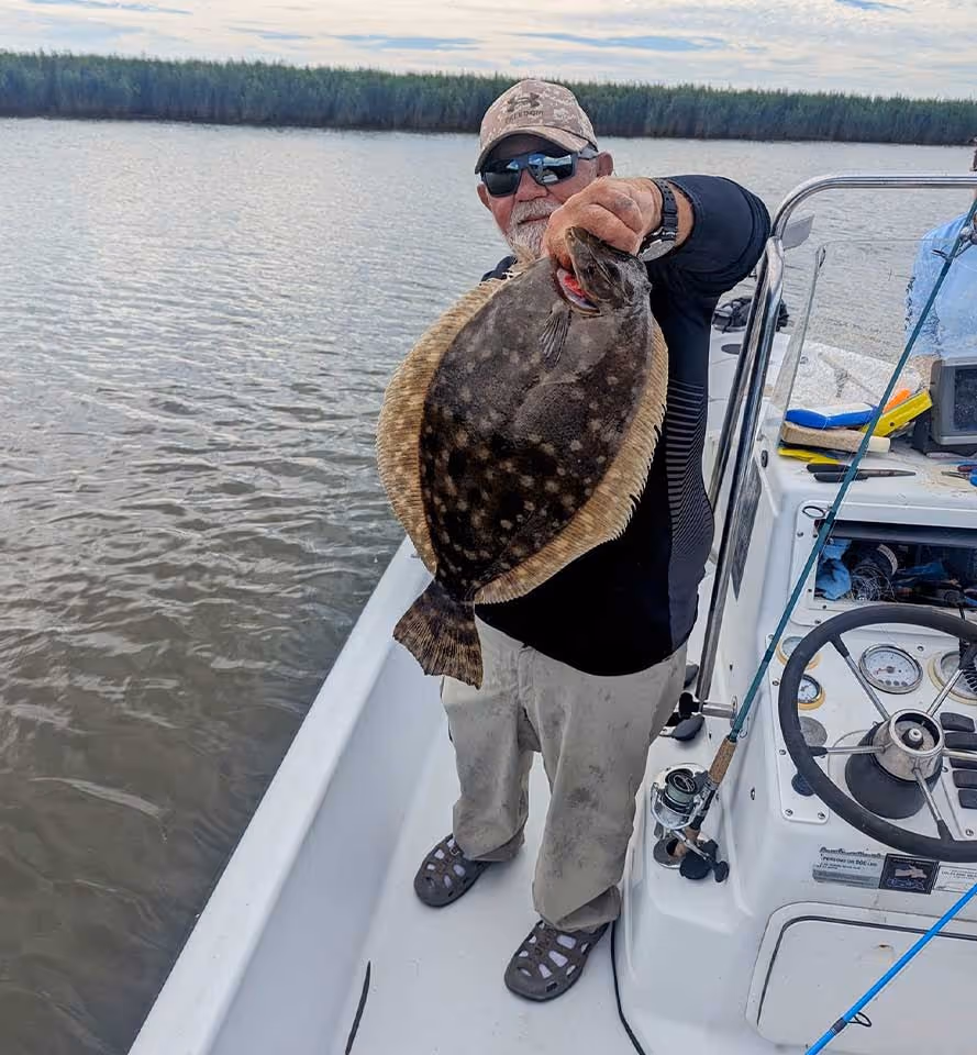 Fisherman holds large flounder on boat with forest background