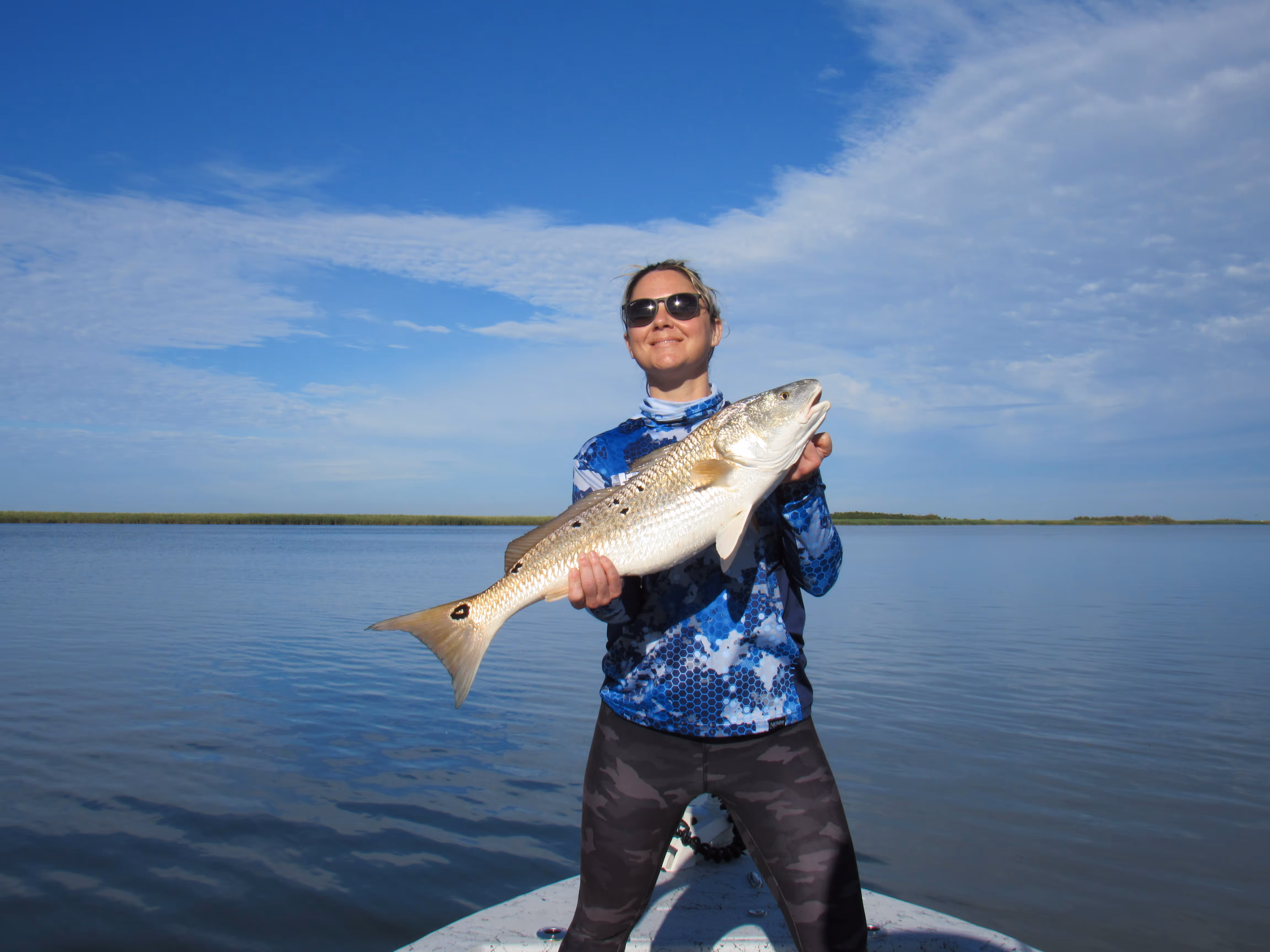 Angler proudly holding large fish on calm water with blue sky backdrop