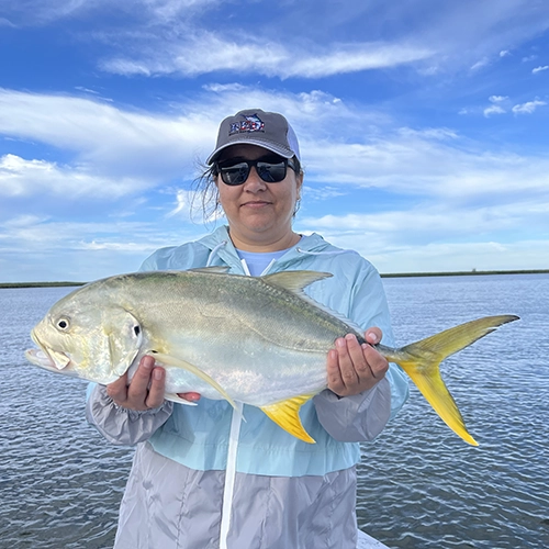 Angler holding large yellow-tailed fish on sunny day near water
