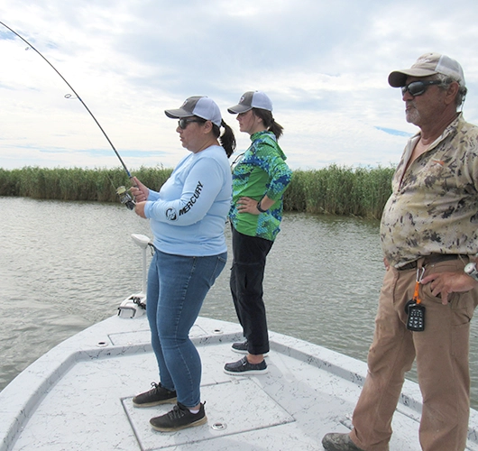 Three people fishing together on a boat in marshy waters