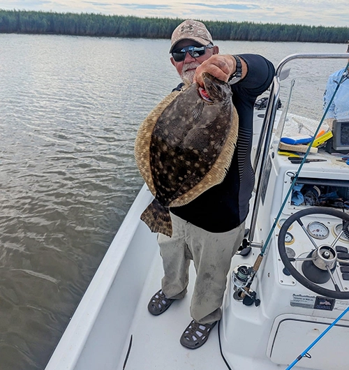 Fisherman holding large flounder on boat with forest backdrop