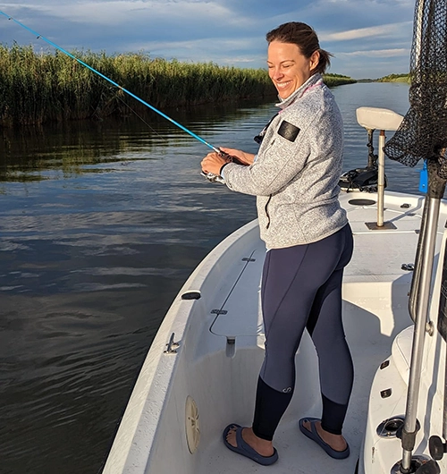 Woman fishing on a boat in a calm lake with reeds and blue sky