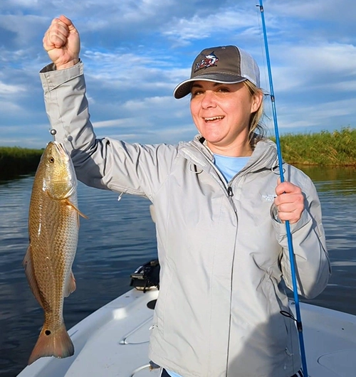 Excited angler holding large redfish on boat with blue fishing rod