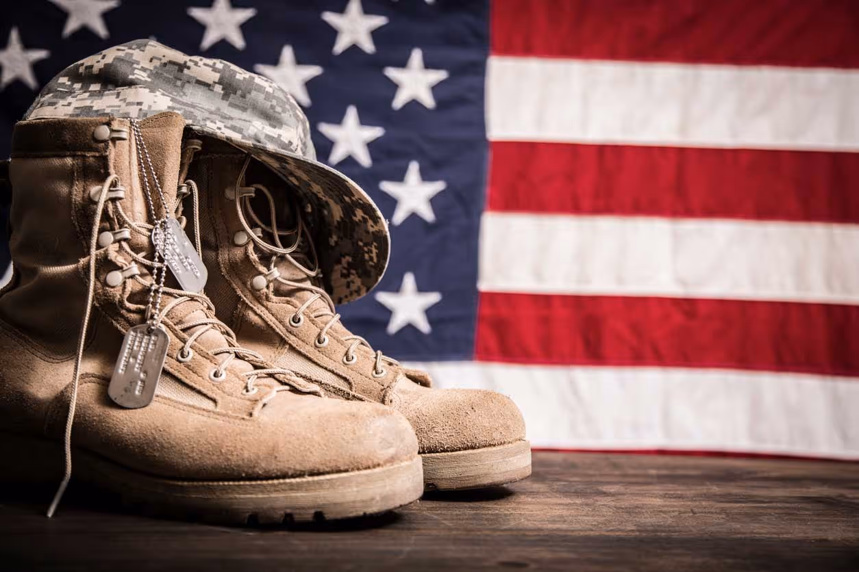 Military boots and dog tags on wooden surface with American flag background