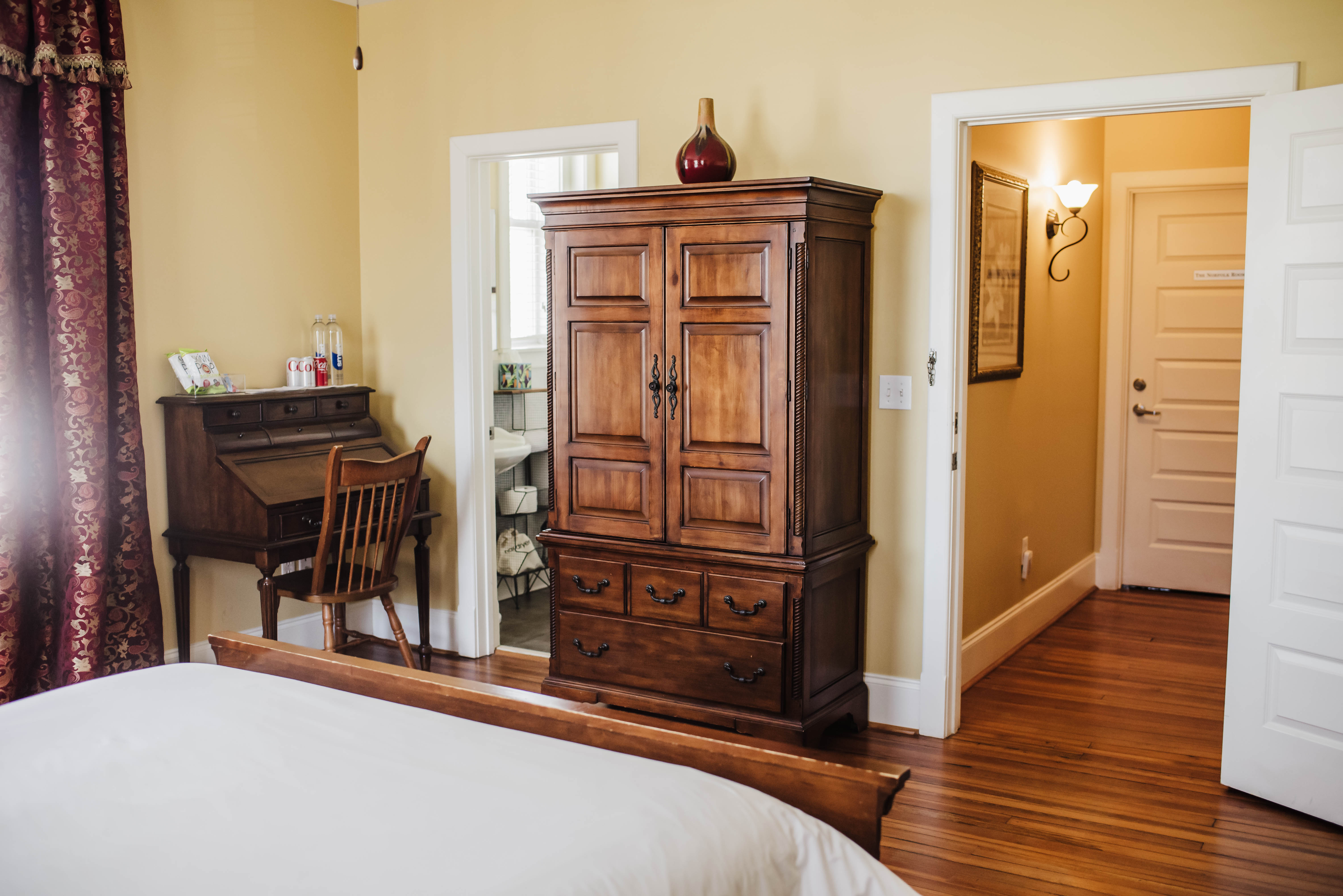 View from the foot of the bed toward the armoire, bathroom, and entry door in The Chezy Room