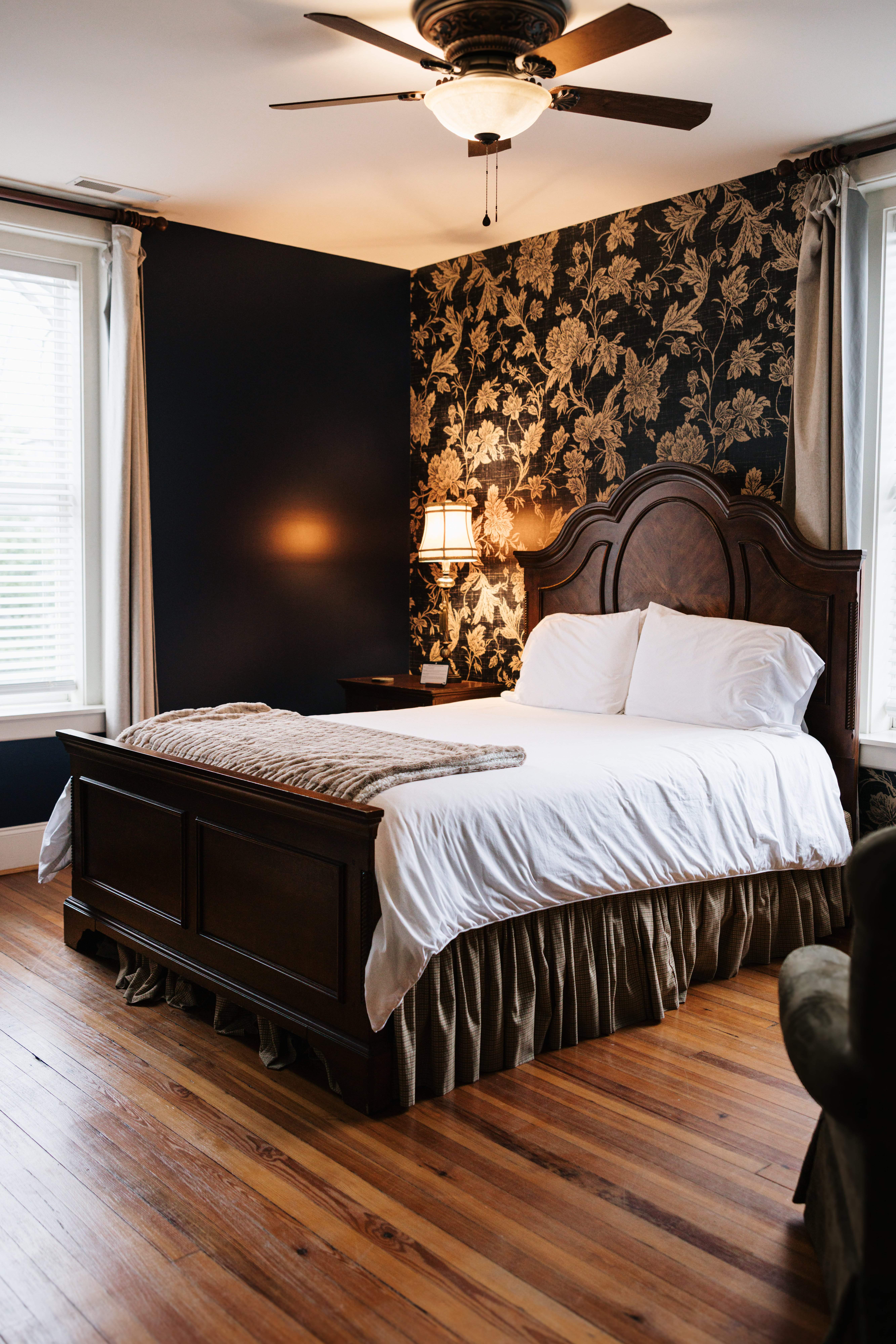 Queen bed in The Georgia Room with dark floral accent wall and ceiling fan
