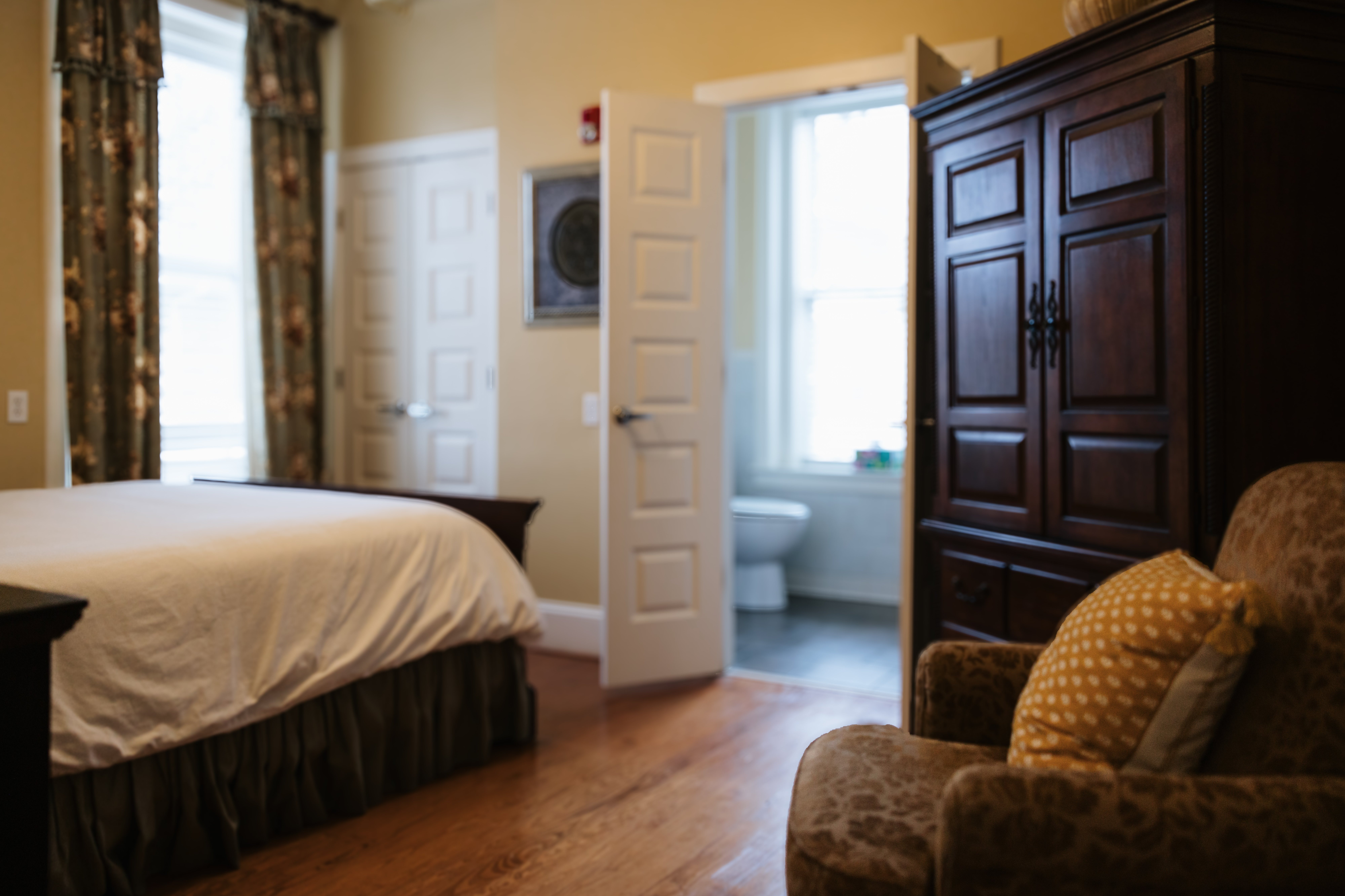 Wide view of The Lyon Room with armoire, armchair, and bathroom door open