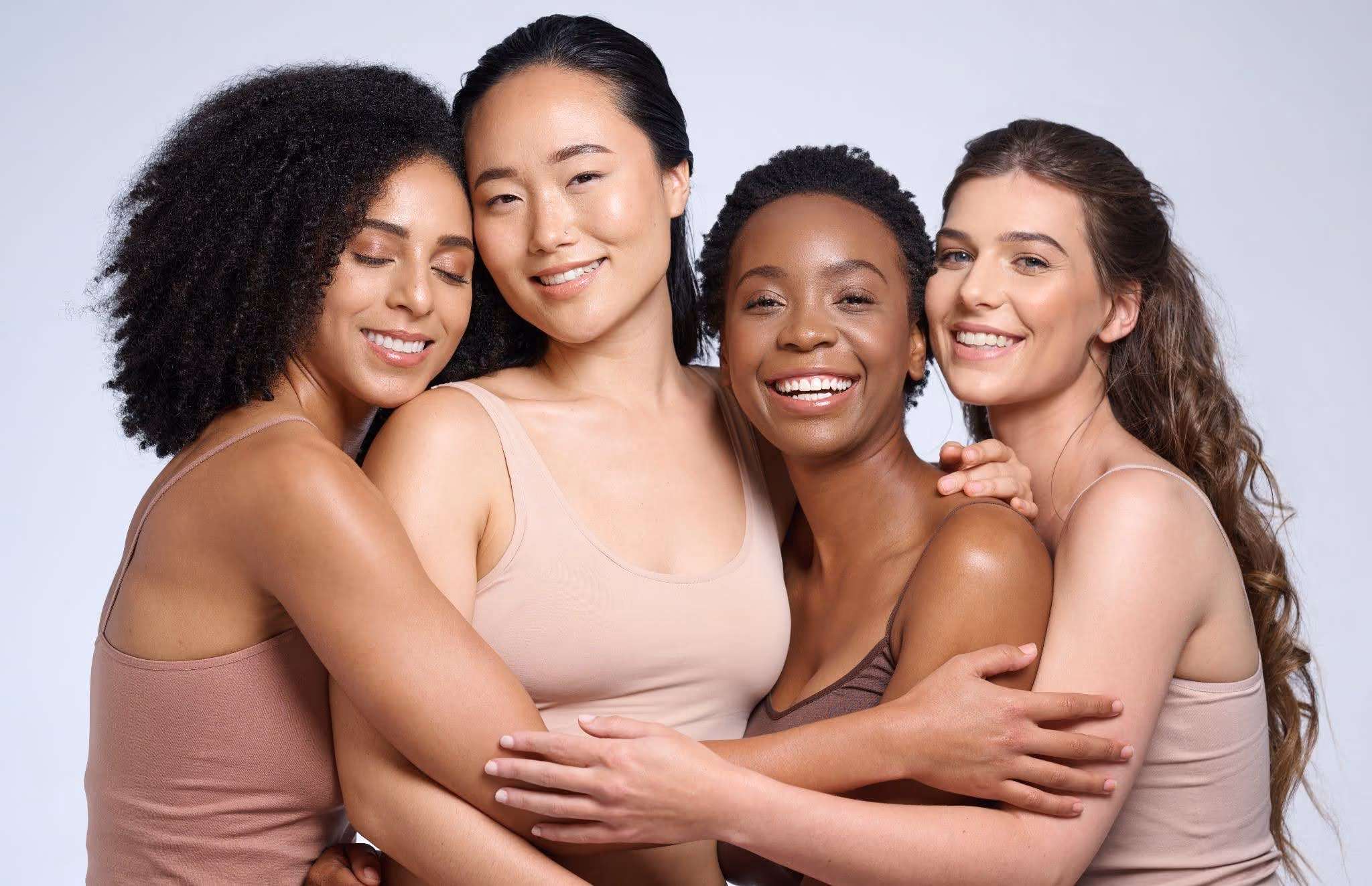 4 women of varying skin tones smile and hug
