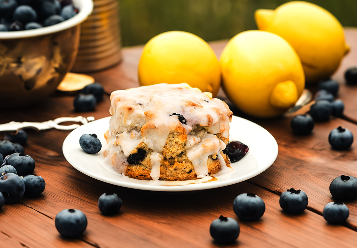 Distinct Indulgence Blueberry Scone on a table surrounded by blueberries and lemons
