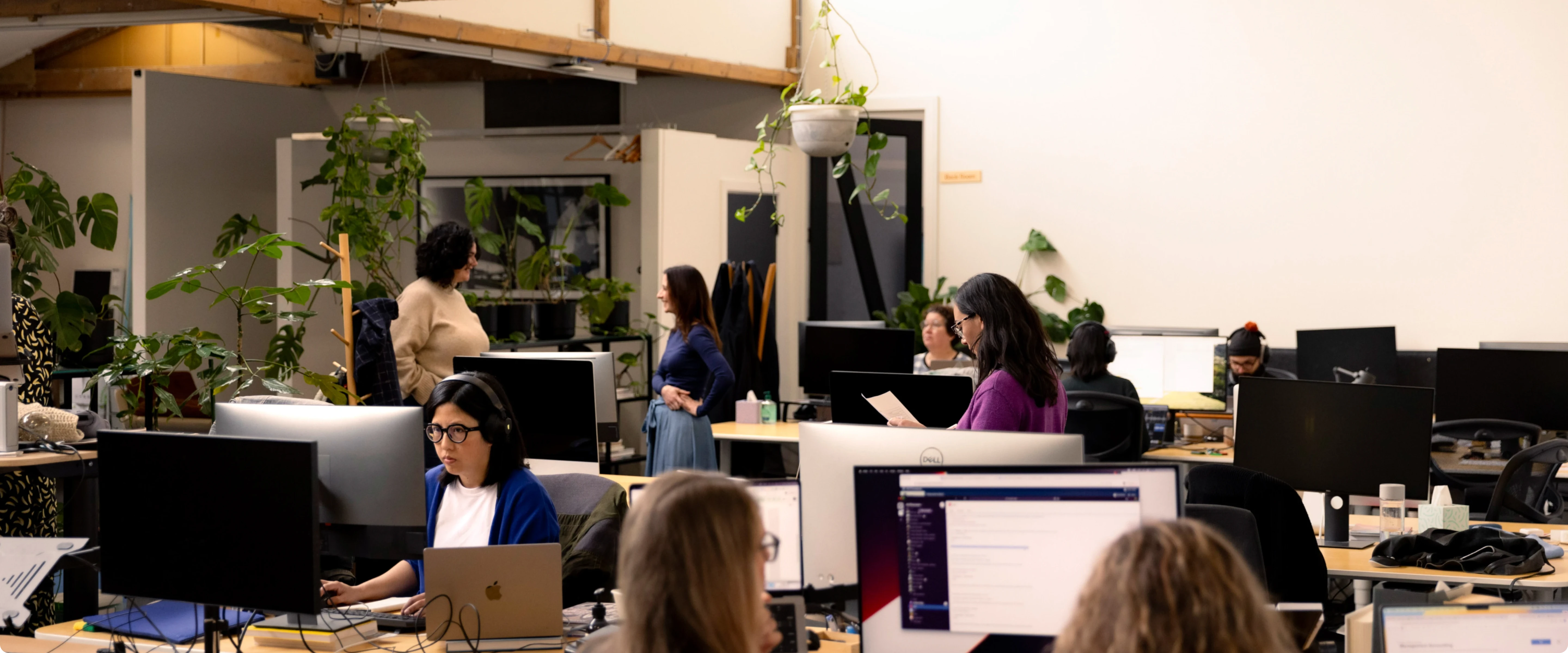 Office scene with team members working at desks with computer monitors in a bright, modern space.