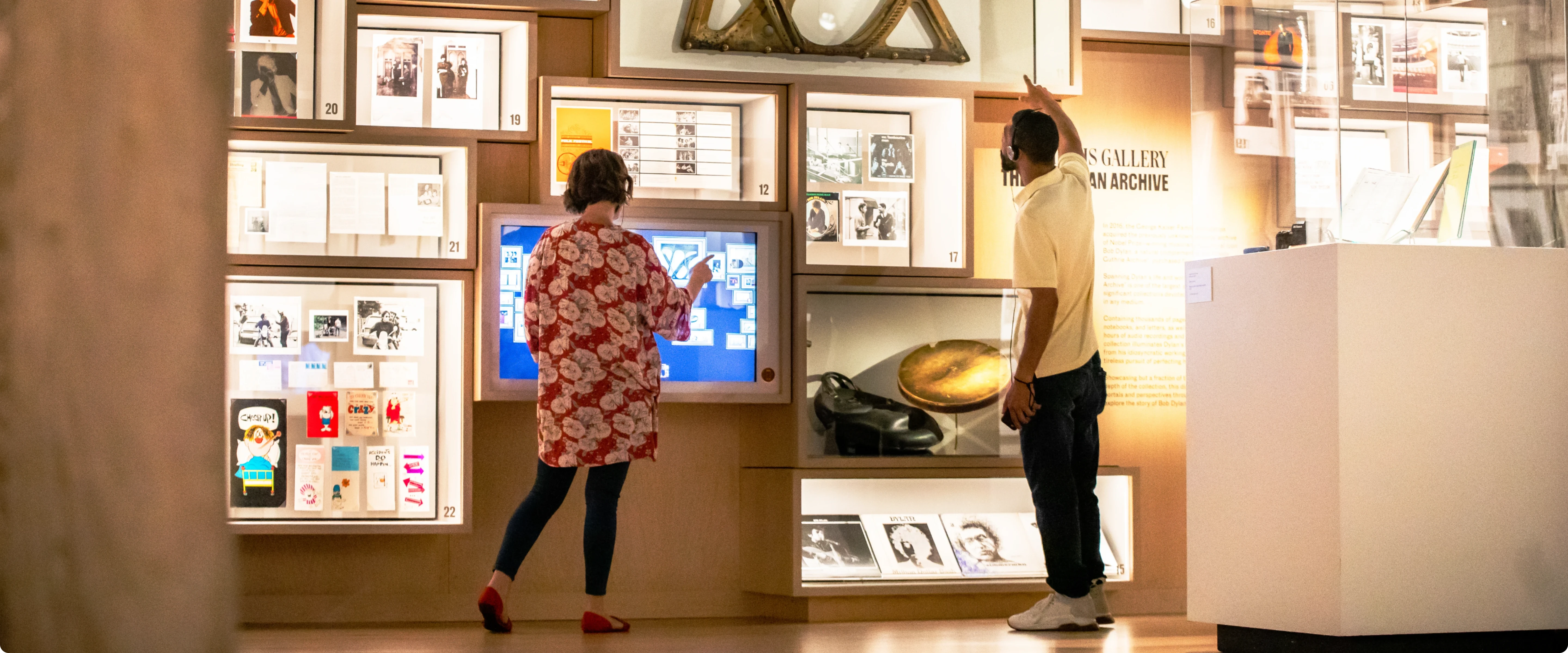 Exhibition space with visitors interacting with digital content and framed artworks on a wall.