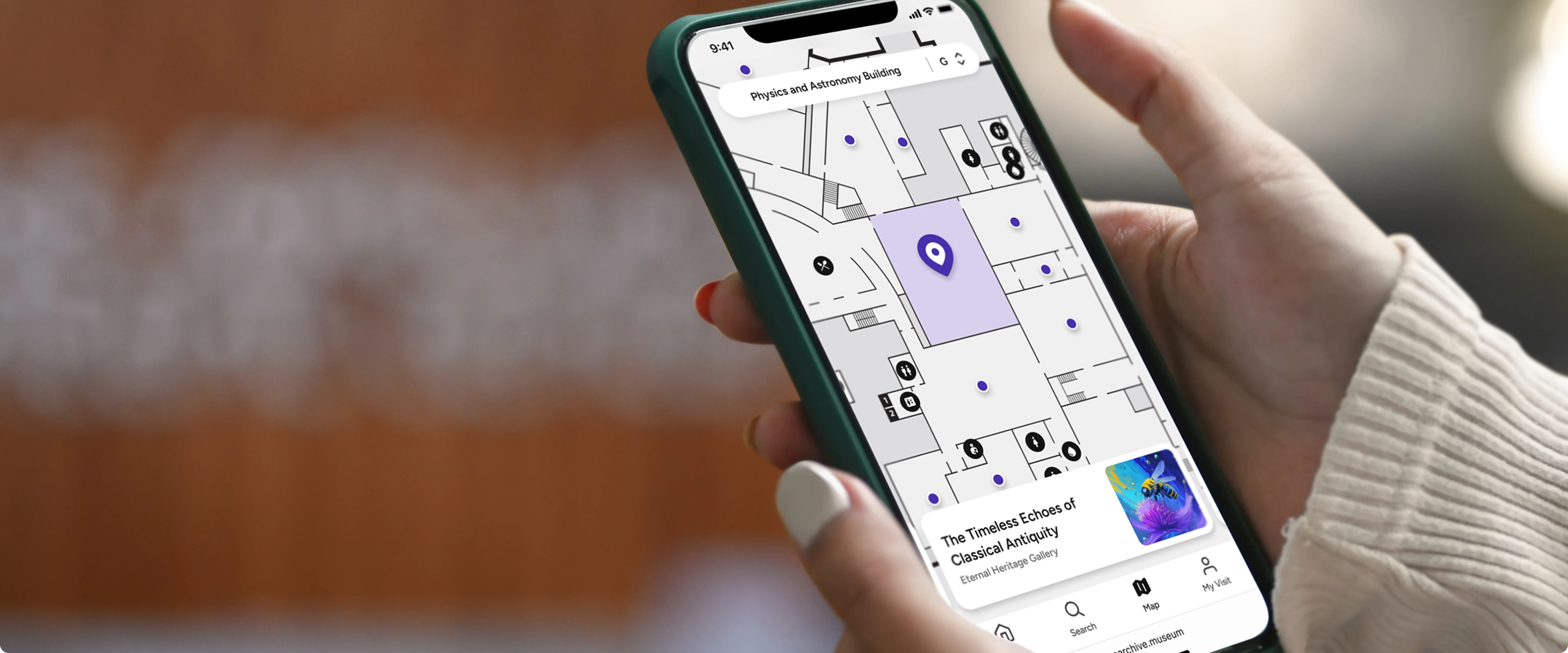 Close-up of a hand holding a smartphone displaying a map and wayfinding route in a museum or gallery setting.