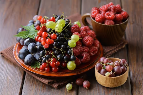 A plate filled with with different types of berries and two bowls besides it filled with raspberries and grapes each