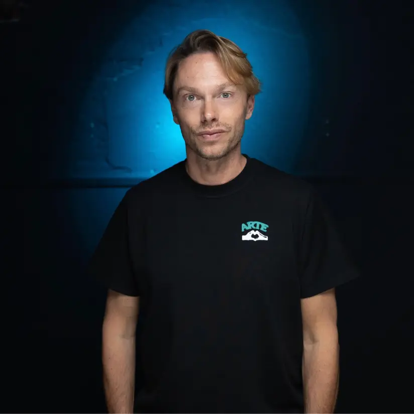 regi boeken die in een portretfoto een zwarte tshirt aanheeft en een blauwe achtergrond