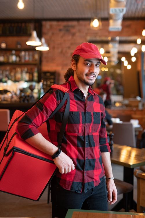 A young and happy blue collar delivery executive holding a delivery bag and smiling into the camera.