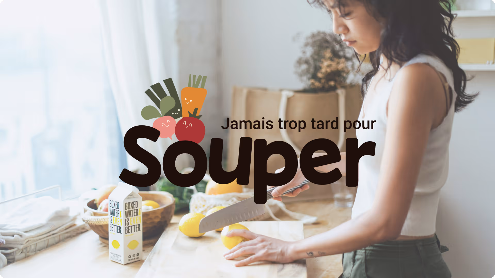 Personne en train de couper des citrons sur une planche à découper dans une cuisine lumineuse avec des cartons d'eau en boîte sur le comptoir.