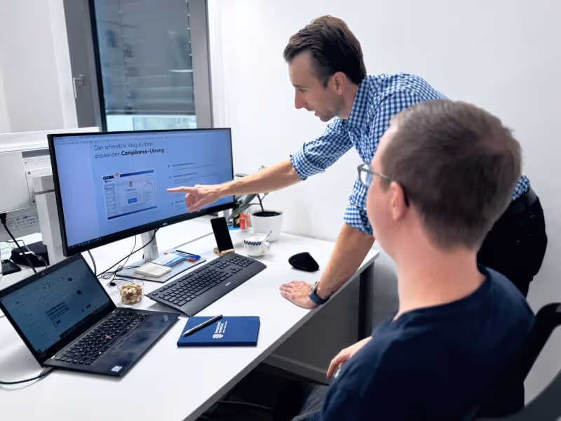 In einem Büro arbeiten zwei Männer zusammen an einem Computer und tauschen Ideen aus.