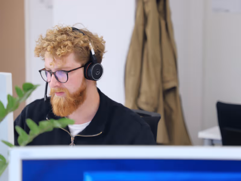 In einem Büro sitzt ein Mann mit Kopfhörern, vertieft in seine Aufgaben.