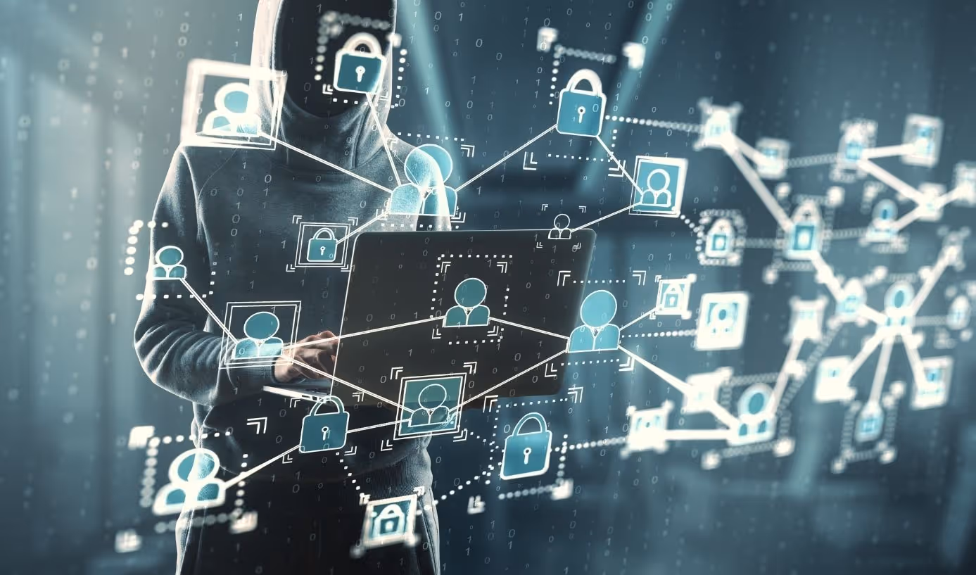 Person in dark hoodie using laptop with floating digital icons of locked padlocks and user profiles connected by lines, representing cybersecurity and data protection.