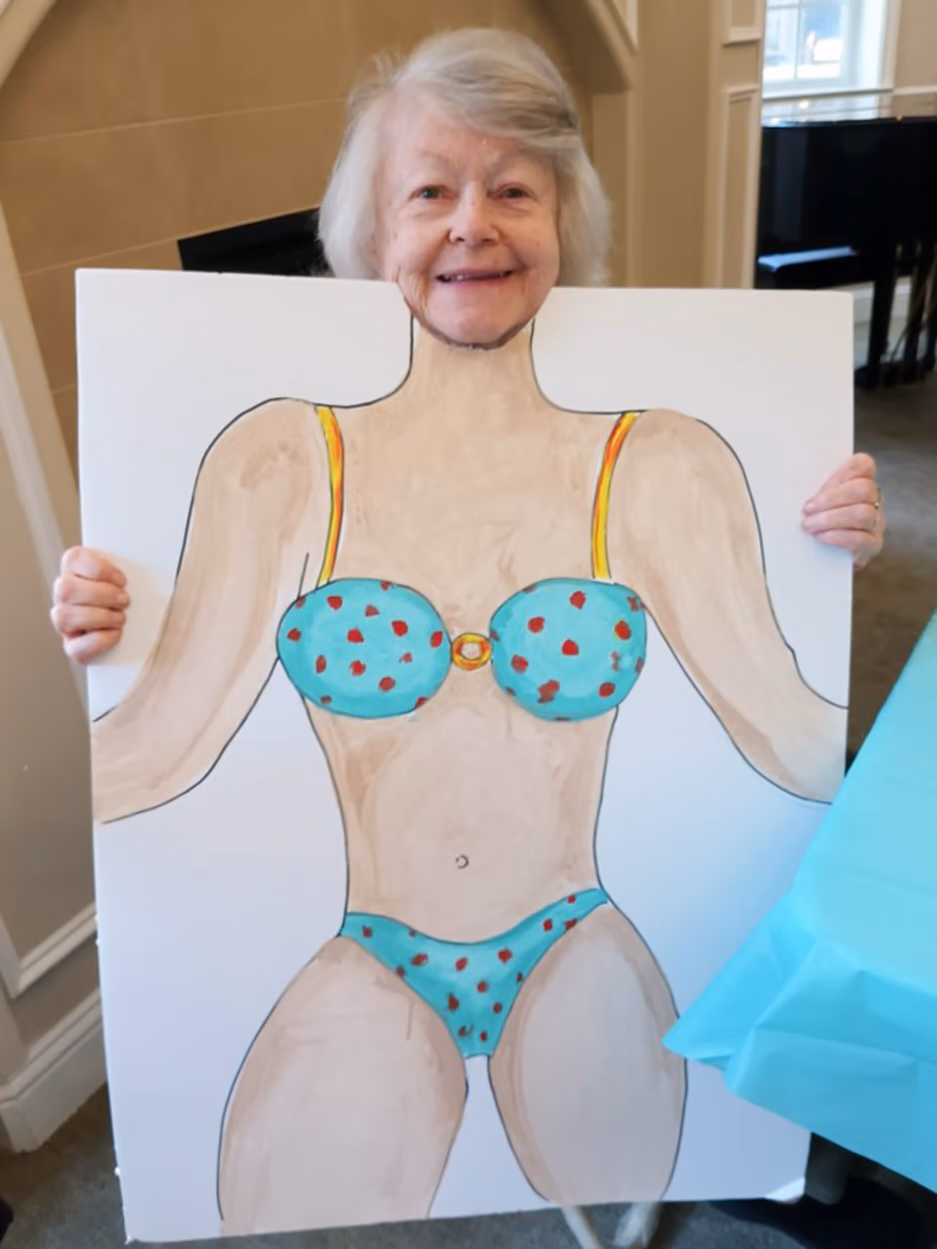 A senior woman playfully poses with a drawing of bikini body.