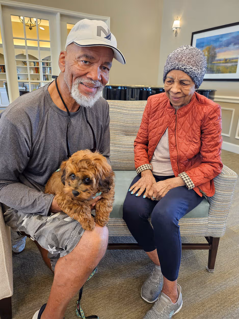 Smiling senior couple sitting on a bench, with the man holding a small brown puppy
