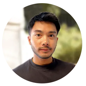 Portrait d'un homme asiatique avec barbe courte, portant un t-shirt noir, fond flou naturel.