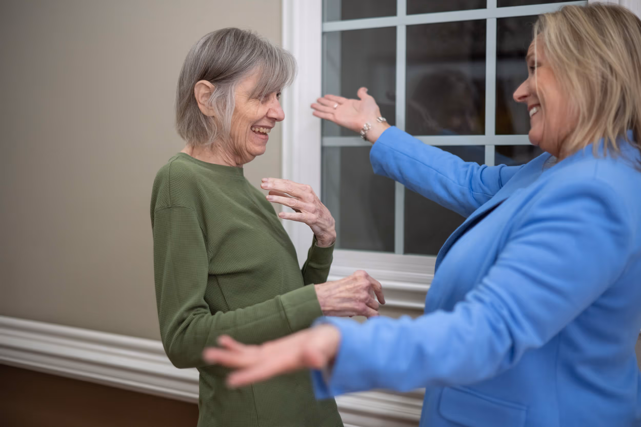 Two women smiling and reaching out for a warm embrace indoors
